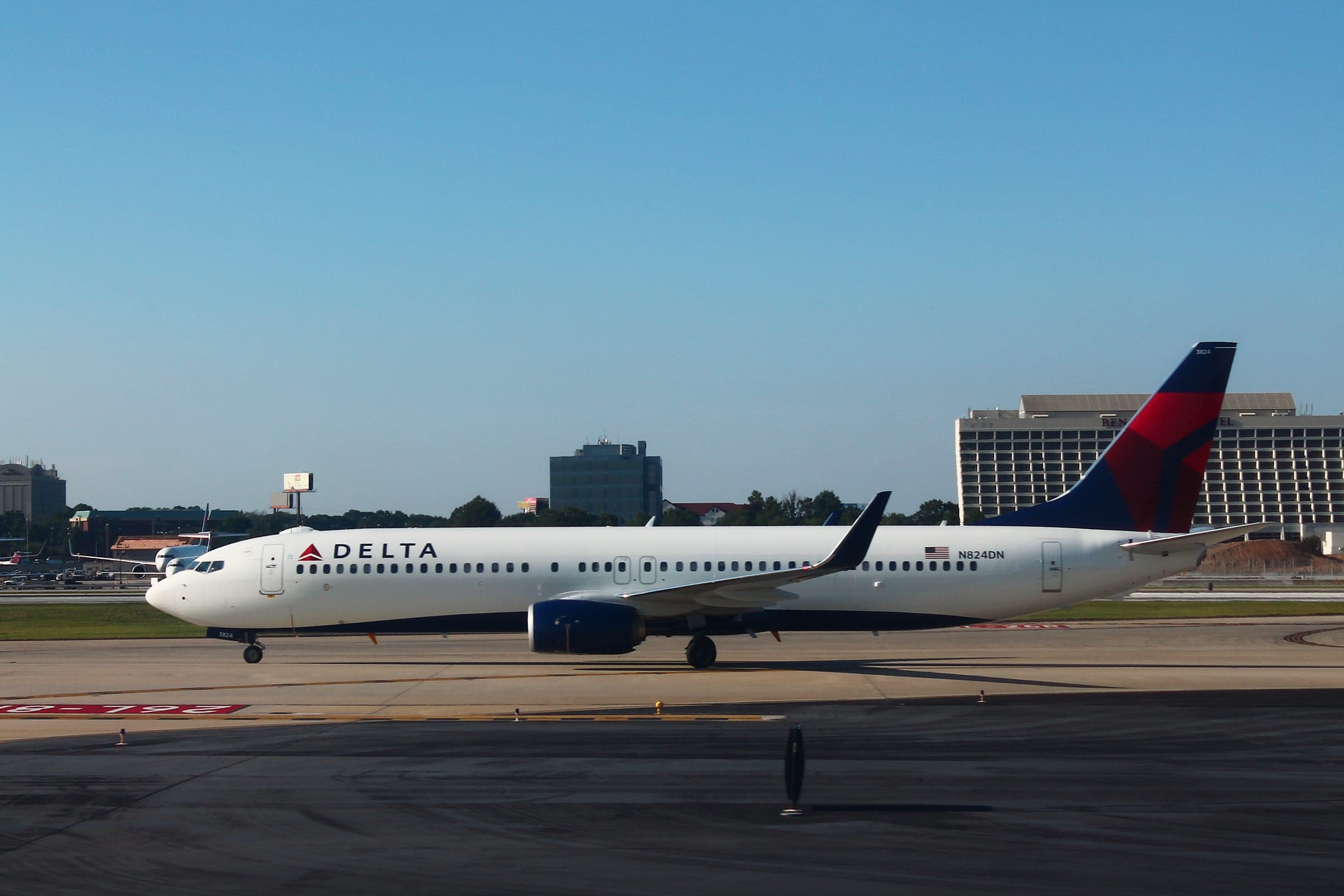 A Delta Air Lines Boeing 737-900 taxiing at Atlanta, the airport hotel and treeline behind it.