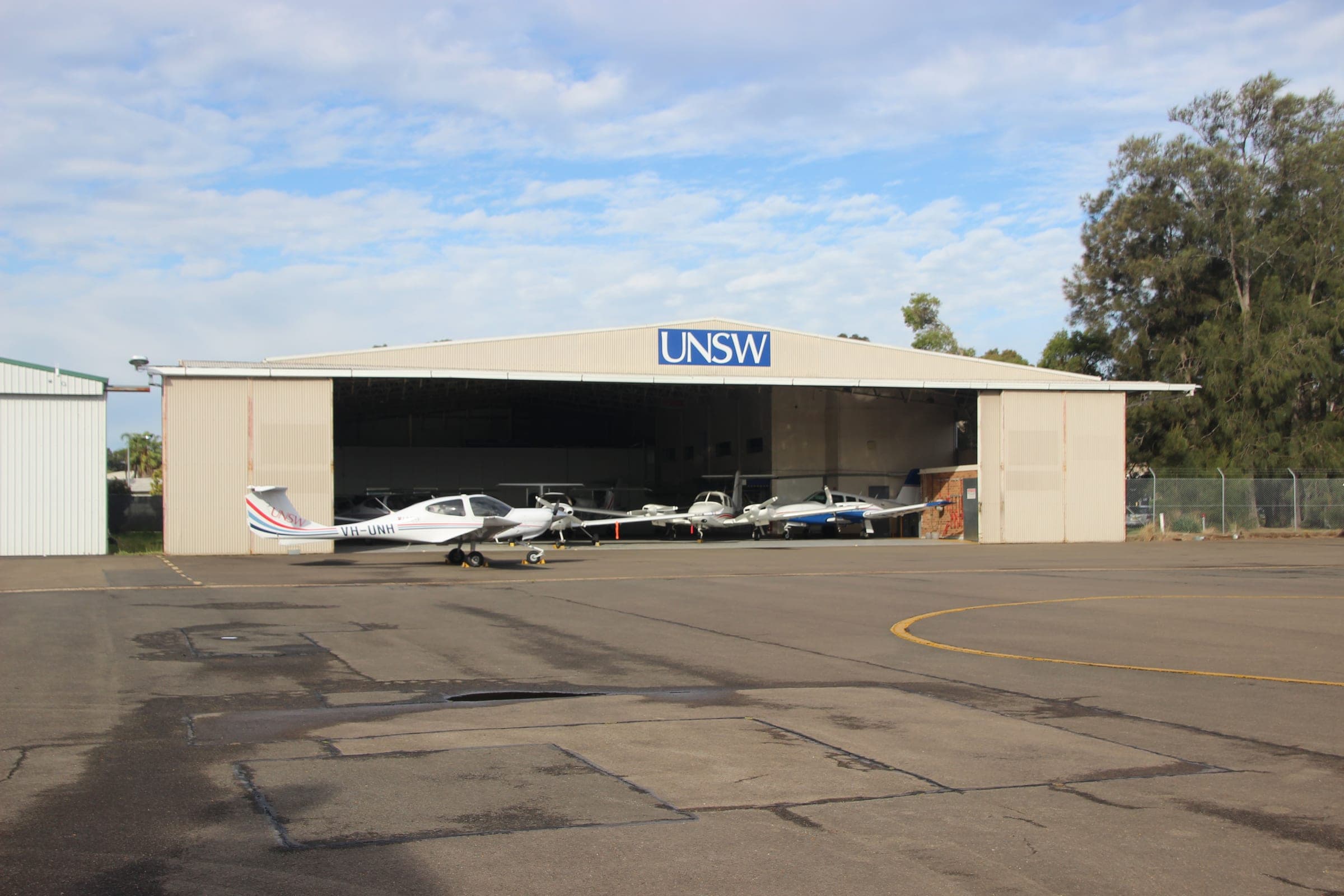 Light training aircraft parked in and around an open flight-training hangar on a quiet apron.