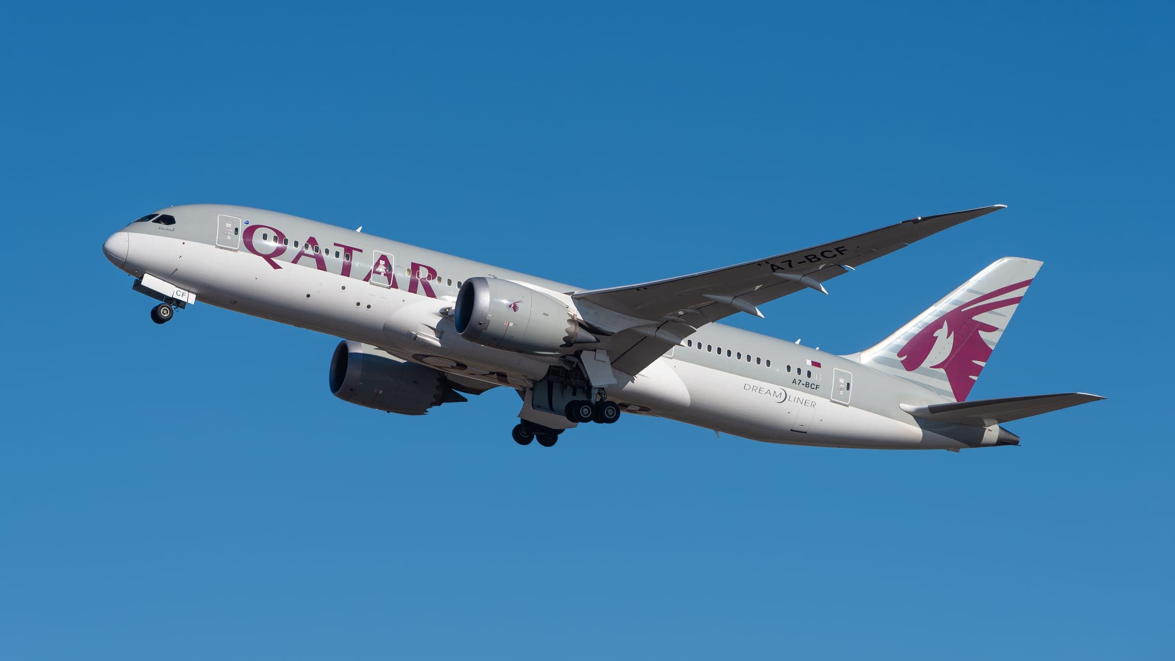 A Qatar Airways Boeing 787-8 Dreamliner, registration A7-BCF, climbing out against a cloudless blue sky.