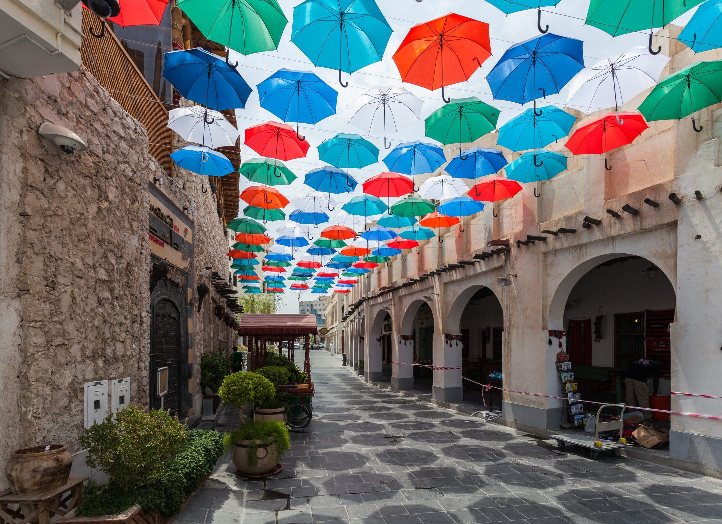 A lane of Souq Waqif in Doha shaded by a canopy of coloured umbrellas.
